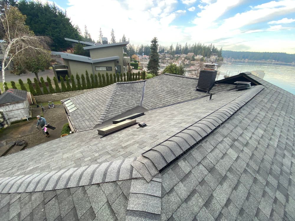 Aerial view of a modern home with a grey shingle roof overlooking a scenic waterfront.