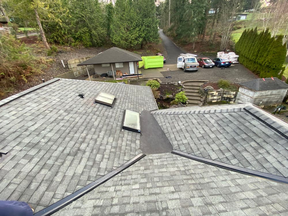 Aerial view of a sloped roof with skylights and nearby parking area in a wooded setting.