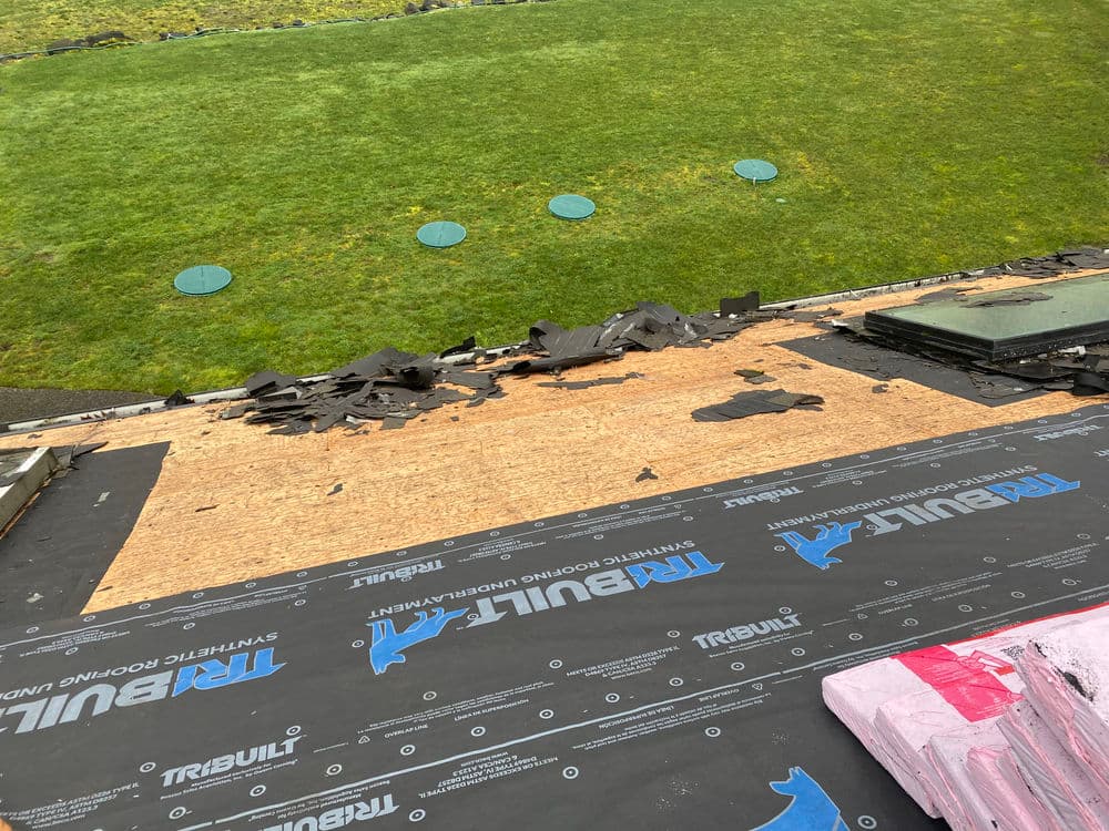 Roof undergoing renovation, showcasing exposed plywood and roofing materials on a grassy yard.