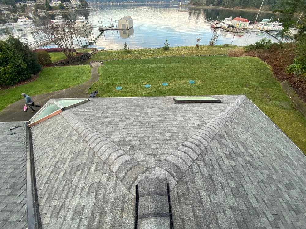 Aerial view of a roof with shingles, overlooking a serene waterfront with boats and greenery.