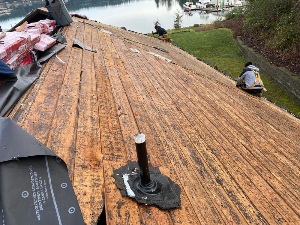 Roofing work in progress with wooden deck, tools, and scenic water view in background.