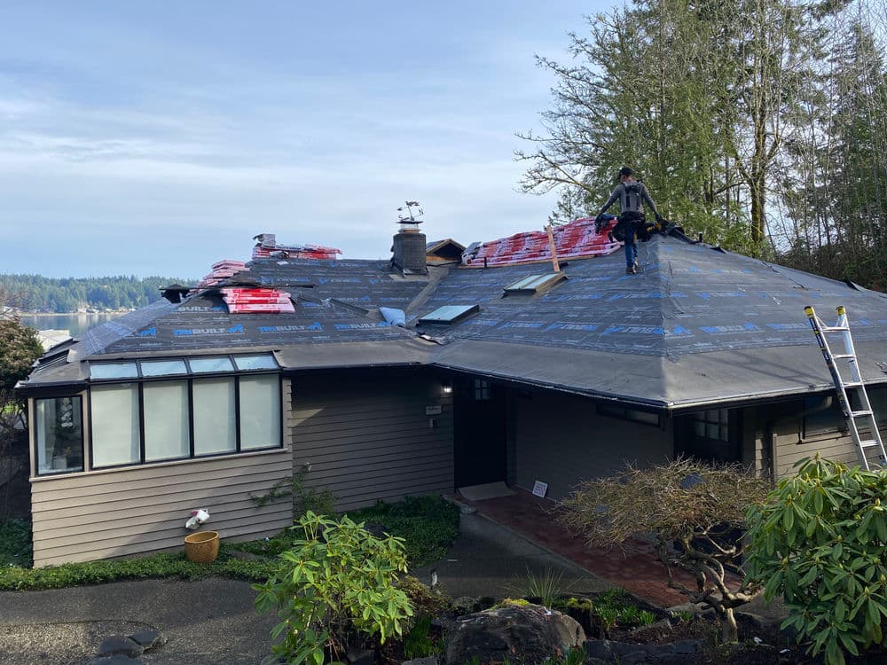 Roof replacement project showing construction worker on a house with roofing materials stacked.