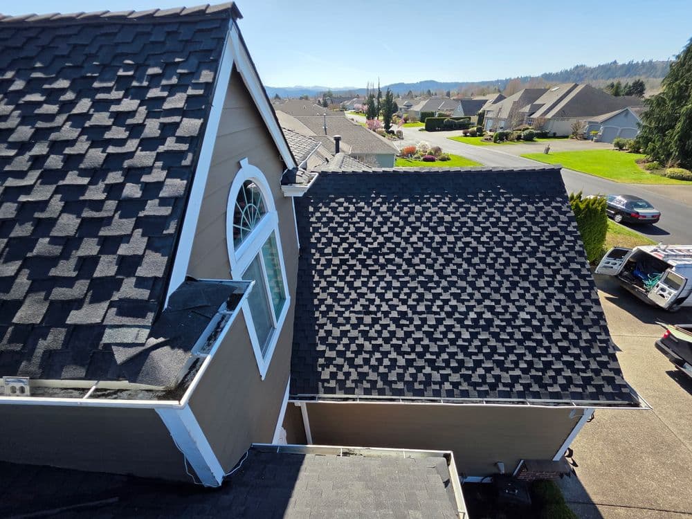 Aerial view of residential roof with black shingles and a clear blue sky.