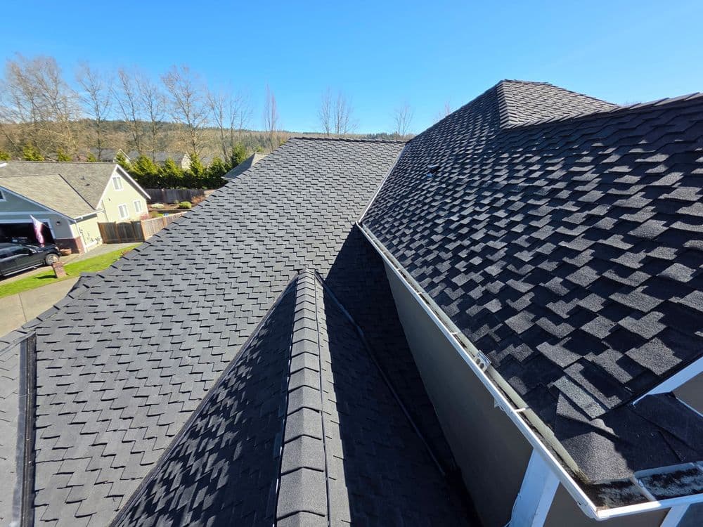 Aerial view of multi-level asphalt shingle roofs under clear blue sky.